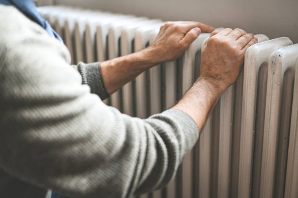 mature adult man warms himself by the radiator in the room stock photo