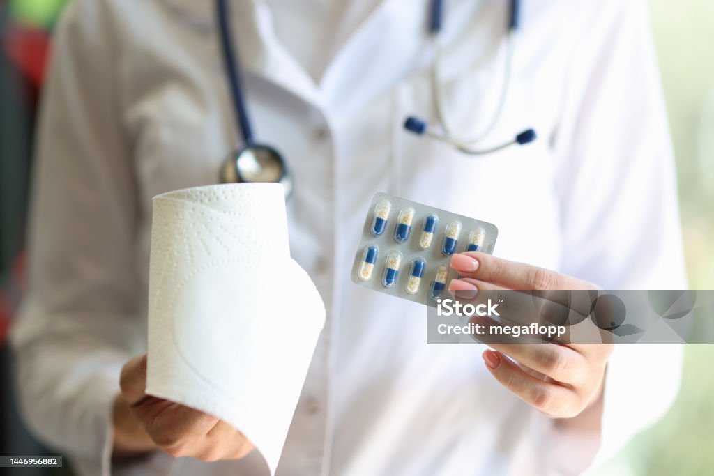 Female doctor holding blister of pills and toilet roll Close-up of female doctor holding blister of pills and toilet roll. Stop diarrhea pills or constipation treatment concept Advice Stock Photo