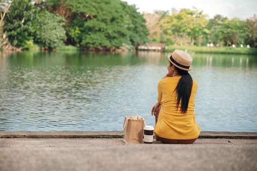Rear view Adult woman holding Reusable coffee cup  while relaxing sitting at public park in the weekend
