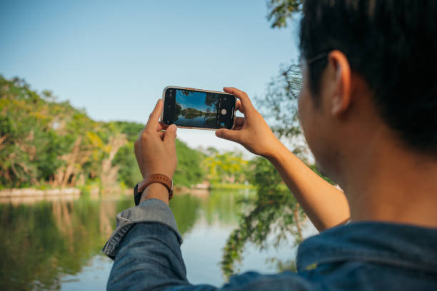 Asian Man using mobile phone taking a photo at park. Environmental Wellbeing