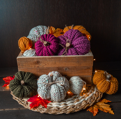 colorful handmade crochet pumpkins in a wooden box with autumn leaves, crochet hook and woolen balls on dark brown wooden ground fall background
