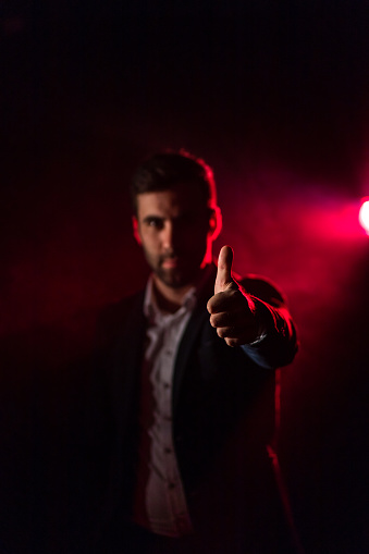 Photo of smiling man showing thumb up on dark background with pink light. Concept of man with thumb up.