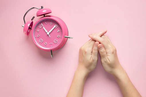 Woman holds hand with a pink alarm clock is waiting time for someone meeting. Late appointment or lunch.