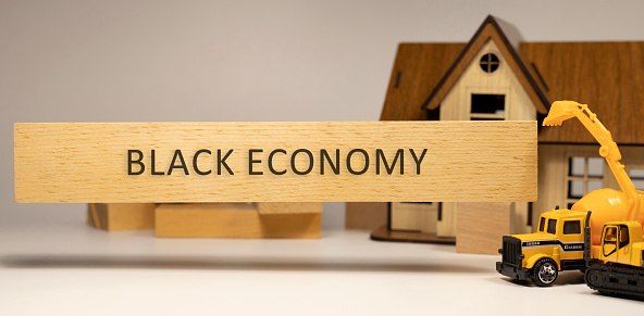 Black economy word written on wooden surface. House and construction concept in background . Mortgage and economy