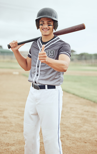 Baseball player, thumbs up and success for sports game on stadium pitch, field and arena for competition match. Portrait, smile and happy softball man with baseball bat, fitness helmet or winner hand