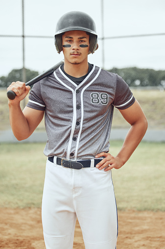 Portrait of baseball player looking focused with warrior paint on his face. Serious fit, active mix race athlete wearing a helmet during a game on a pitch. Sporty man holding a bat before playing a match