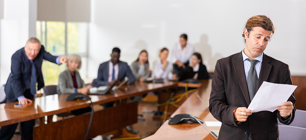 Selective focus shot of smiling young businesswoman sitting at conference table with her colleagues and carefully listening to manager, off screen, leading a meeting.