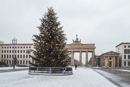 a colorfully decorated Christmas tree stands in front of the Brandenburg Gate in Berlin