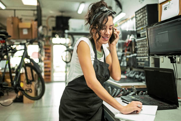 Beautiful young female bicycle mechanic talking to a customer using phone stock photo