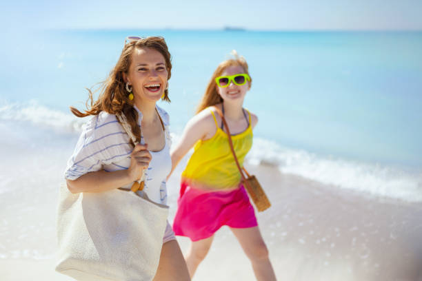 улыбающаяся стильная мама и дочь-подросток на прогулке по пляжу - teenager parent beach contemporary стоковые фото и изображения