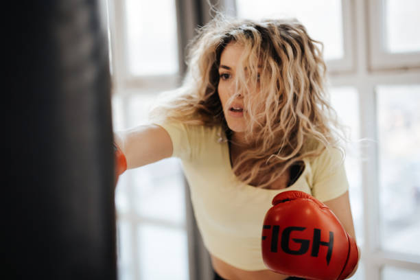 Young female boxer training with punching bag in the gym Young female boxer training with punching bag in the gym boxing gym stock pictures, royalty-free photos & images