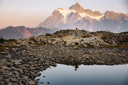A Caucasian woman enjoys a hike on a beautiful Autumn day in Mount Baker area, Washington state, USA.  She walks along. a ridge line, watching the setting sun and view of Mount Shuksan. Healthy and enjoyable lifestyle.