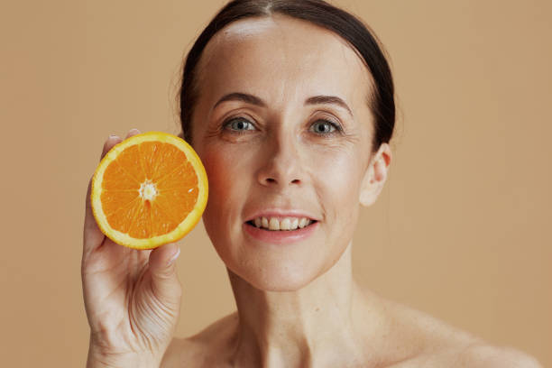 istock smiling modern female with orange isolated on beige 1446974311