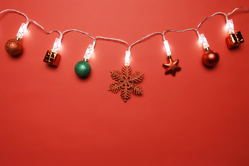 Christmas lights with Christmas ornaments on the red background with copy space