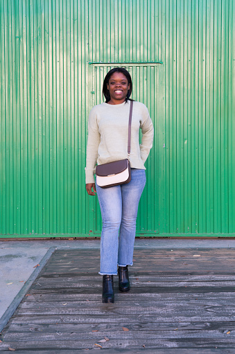 Portrait of smiling african american woman in white sweater near green door outdoors. Smiling African American woman in white sweater on the sidewalk with a green door in the background.