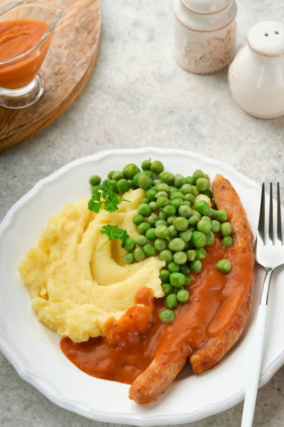 bangers und brei. grillwürste mit kartoffelpüree und grünen erbsen auf weißem teller auf grauem grund. traditionelles gericht aus großbritannien und irland. bbq rindfleischwürste. draufsicht. - mashed potato food staple vertical color image stock-fotos und bilder