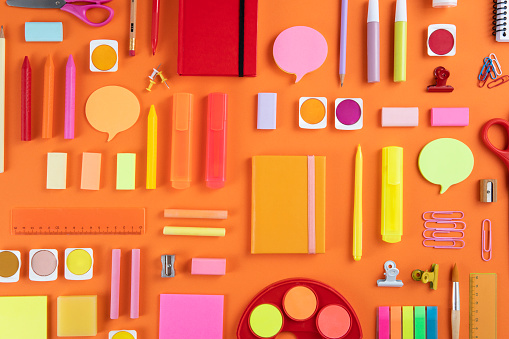 Back to school concept with crayons and school supplies on orange colored background