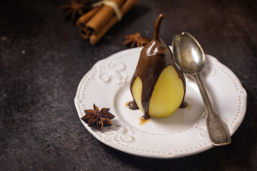 Poached pears glazed with dark chocolate on the dark rustic background