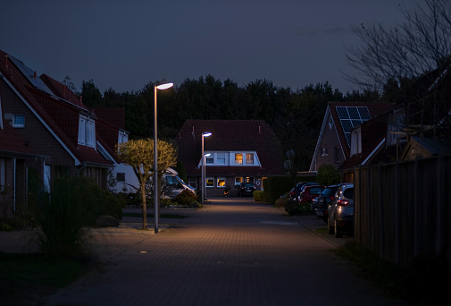 a view of a street at night, lights from houses and parked cars.