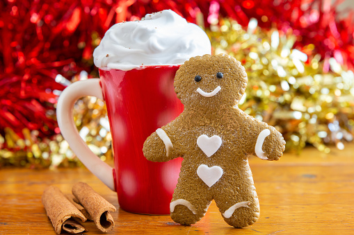 A delicious, home made Gingerbread man at Christmas with comforting warm drink, topped with cream.  Festive background, space for copy.  Horizontal.