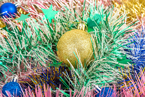 Close up Christmas tree toy ball of golden color among New Year's tinsel. Abstract background or texture.