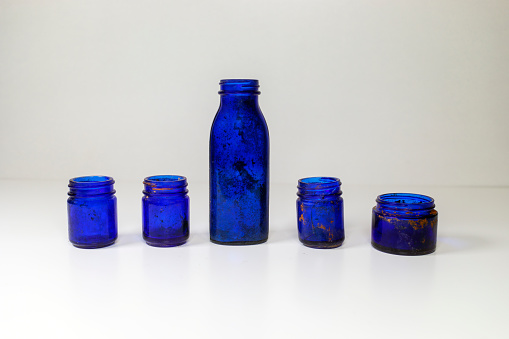 Aged and patina vintage blue glass medical bottles on a white and gray background with copy space and a rusted cap.