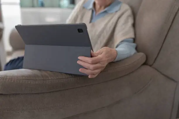 An old woman is sitting on a couch and holding a tablet
