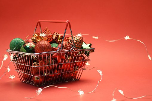 Christmas shopping concept. Christmas ornaments and Christmas lights in the shopping basket on the red background with copy space