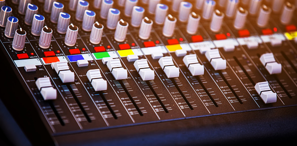 sound mixer with coloured controls and sliders illuminated by stage lights ready for music concert