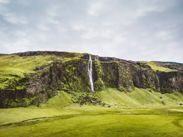Photo of Drifandi waterfall in Iceland, grass field and a cliff with waterfall behind