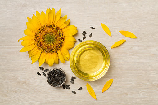 Sunflower oil, seeds and flower on wooden background, top view.