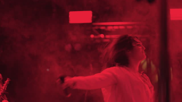 singer girl is dancing on scene during concert of modern rock band, active red lights strobing, portrait