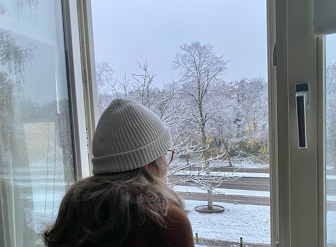 Beautiful woman is watching the snowfall in the morning