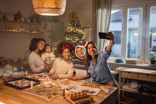 Female gay couple with kids having fun for Christmas at home. They are baking cookies in kitchen.