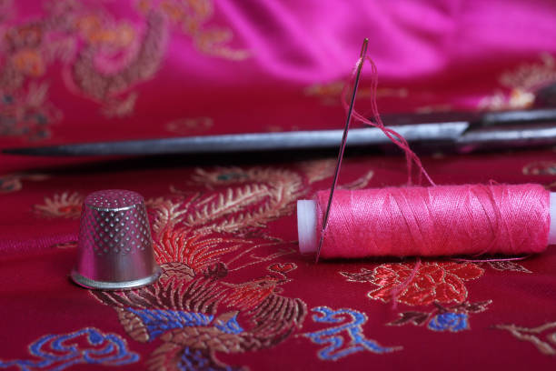 istock Spool of Pink Thread and Thimble on Vintage Pink Satin Fabric 1447004232