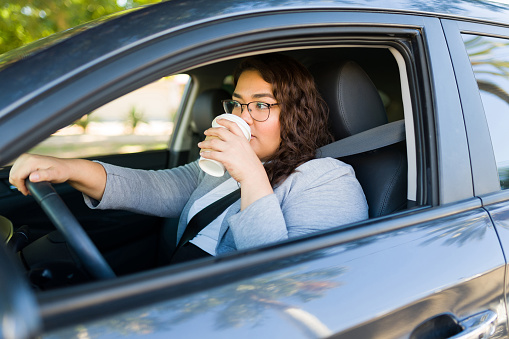 Hispanic attractive obese woman drinking coffee to go and driving her car while commuting to work in the morning