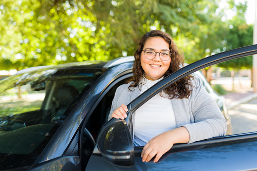 Portrait of a cheerful fat woman opening the car door and smiling while ready to travel by car and drive
