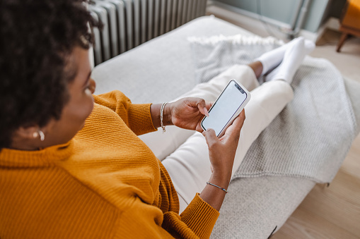 Shot of a young African-American woman in the living room using a smart phone