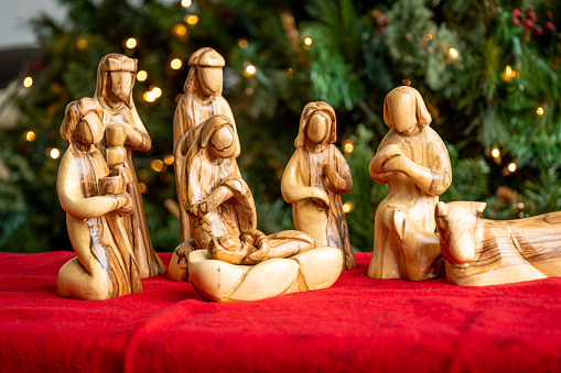 Nativity creche made of olive tree wood from the Holy Land with a Christmas tree and lights background with baby Jesus