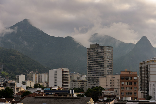 The cloud-shrouded Andaraí Maior  and Perdido peaks and the Atlantic rainforest of Tijuca National Park towering above neighboring districts of the Zona Norte, or North Zone of Rio de Janeiro, Brazil