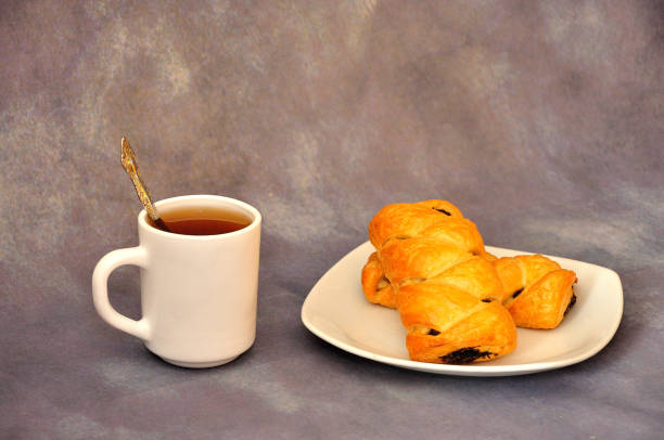 A plate with two puff pastries with poppy seeds and a cup of hot drink on a gray abstract background.