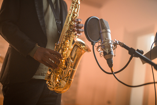 Black mid-adult male musician playing saxophone and recording songs in recording studio. Close-up shot, unrecognizable person.