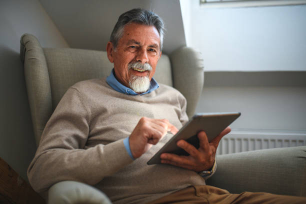 istock Candid Portrait of White Senior Man Looking at Camera while Holding a Digital Tablet 1447036155