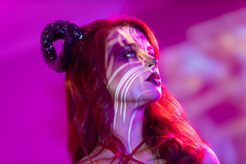 Beautiful young woman with makeup zodiac signs of Aries sign horoscope. Girl with horns on head in neon light.