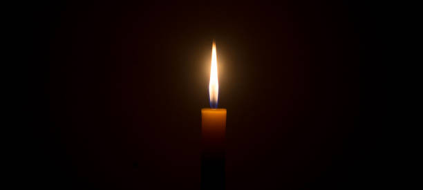 istock A single burning candle flame or light glowing on a white candle on black or dark background on table in church for Christmas, funeral or memorial service 1447042534