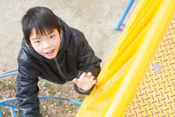 A boy is playing playground. He is just climbing a plaything. He looks up and holding his arm up.
