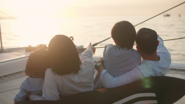 Rear View Of Parents With Sons On A Yacht At Sunset