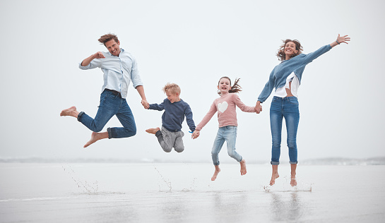 Family, funny and jumping on the beach together while on holiday. Happy family with children, parents and holding hands and jump, fun and smile with love during travel vacation in the Netherlands