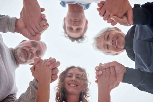 Family, below and holding hands in circle with smile, love and bonding together outdoor. Mom, dad and grandparents with support, unity and trust for care, happiness and help while happy on vacation