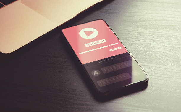istock Video Advertising - digital marketing business concept. Targeting programmatic advertising, native social marketing online media ad strategy. Phone lying on wood table with video ad block on screen 1447053528